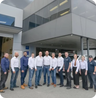 Group of 14 professionals posing for a team photo outside a modern office building with glass and metal exterior.