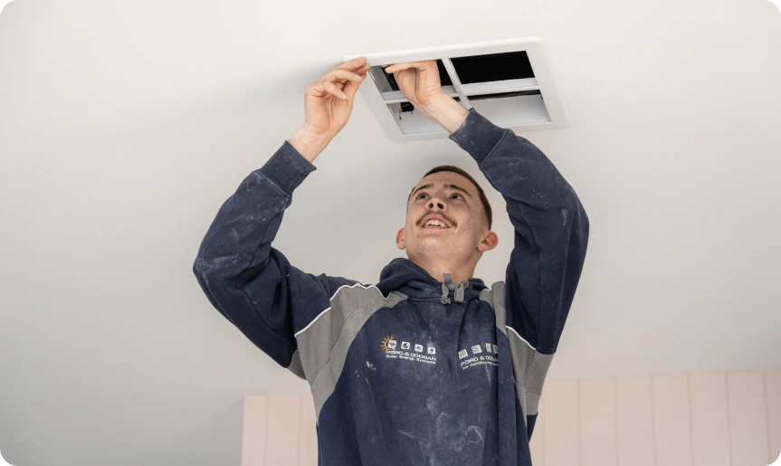 Technician in a dusty uniform installing a ceiling vent.