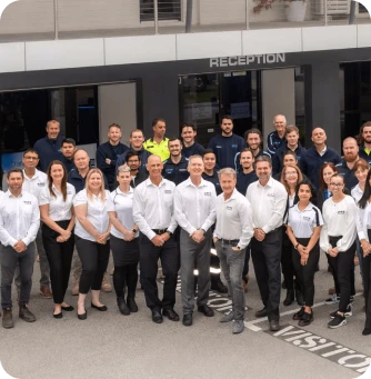 Group of diverse coworkers posing for a photo in front of a building with a reception entrance visible above them.