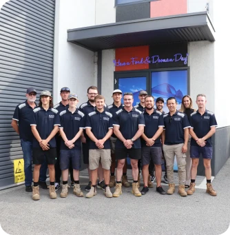 Group of 16 staff in matching navy polo shirts and boots, posing outside a building for a team photo.