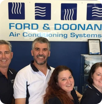 Four smiling technicians pose in front of a blue Ford & Doonan Air Conditioning Systems sign.