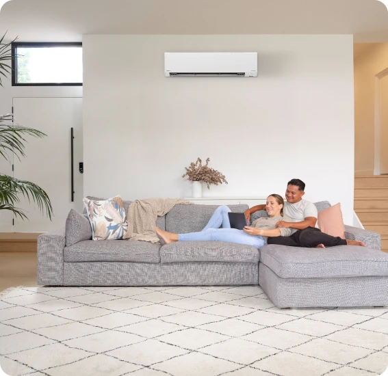 Couple relaxing on a light gray sectional sofa in a modern living room with an air conditioner above.