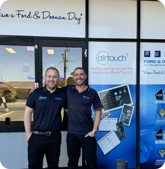Two smiling men in navy polo shirts pose in front of a shop with Airtouch branding and Ford service signage.